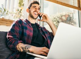 Person smiling while talking on the phone and using a laptop